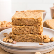 A stack of peanut butter blondies on a plate with some peanuts.
