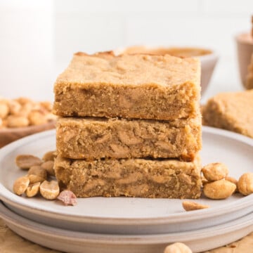 A stack of peanut butter blondies on a plate with some peanuts.