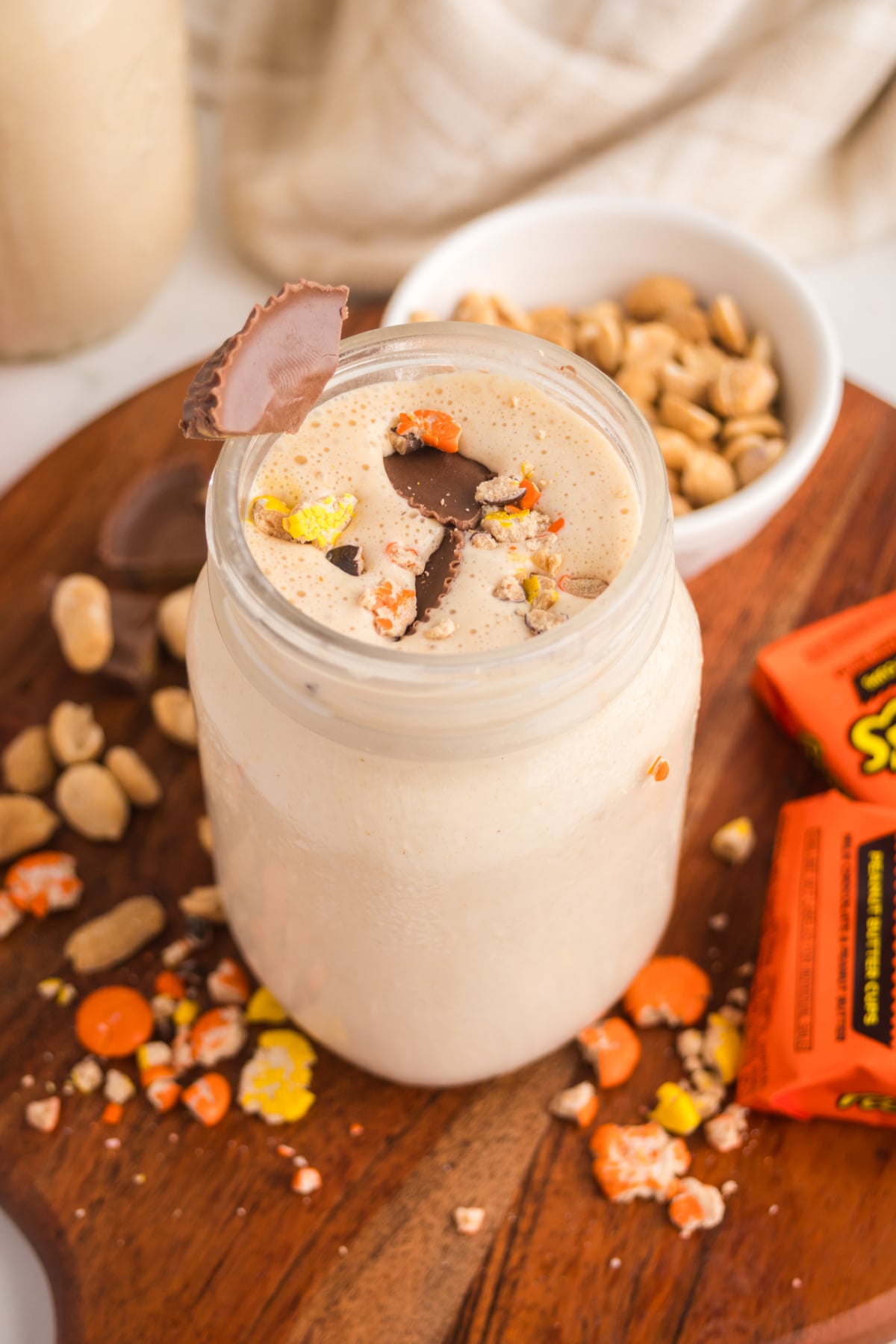 A milkshake in a jar with a sprinkling of Reese's pieces and chopped peanut butter cups on top on a table.