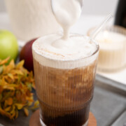 A glass of apple crisp cold brew with apple crisp cold foam being drizzled on top.