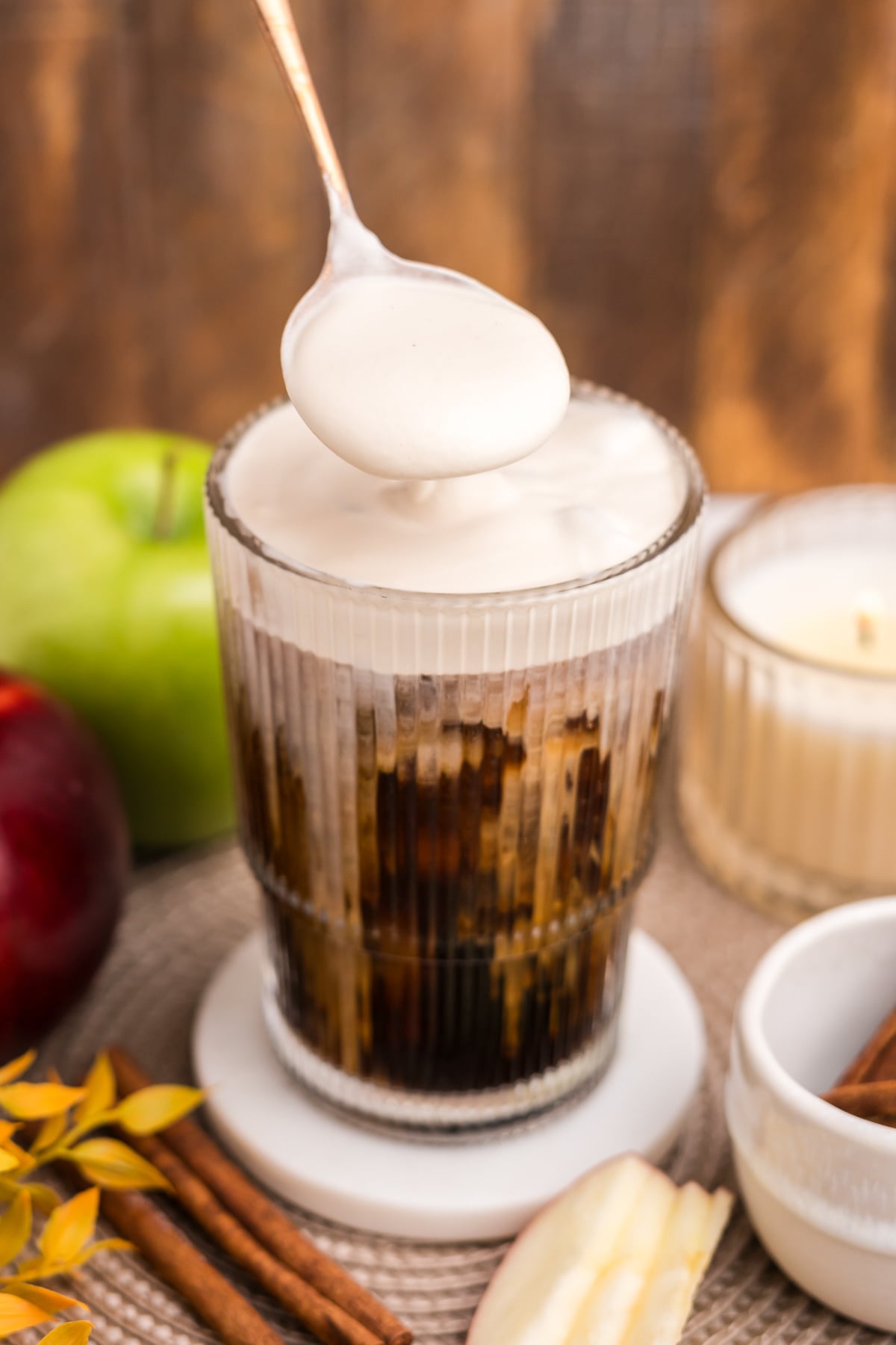 Apple Crisp Cold Foam being spooned onto a glass of iced coffee.
