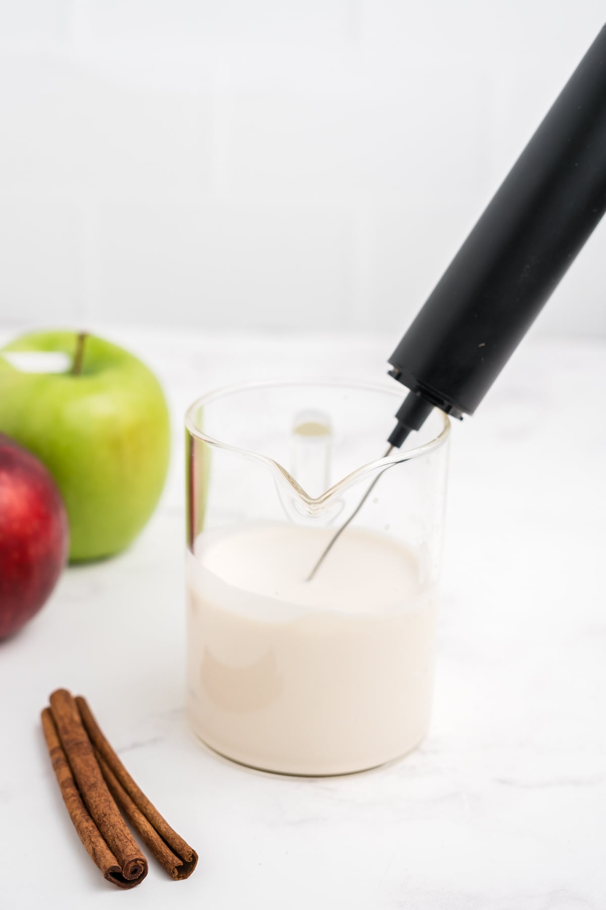Handheld milk frother blending Cold Foam in a tall measuring cup.