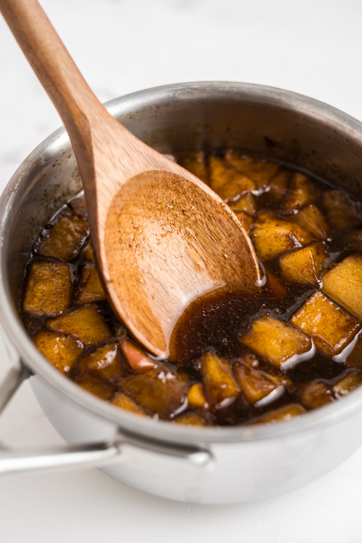 Simmered ingredients in saucepan with a wooden spoon stirring.