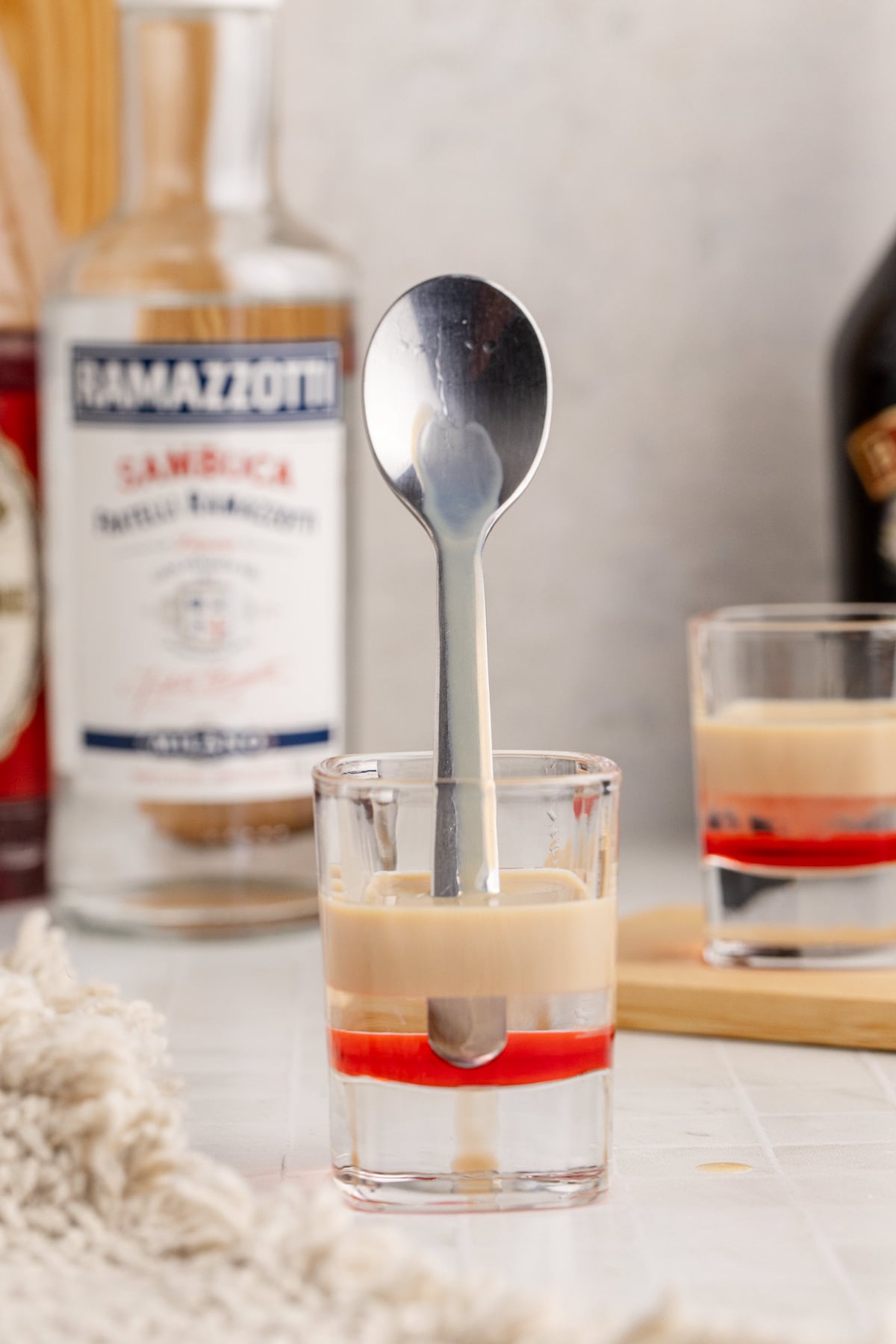 Sambuca and Baileys added to shot glass pouring against a spoon to create layers.