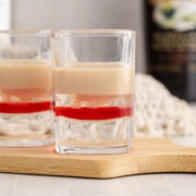 A Baileys Shooter on a cutting board on a table with a shooter and bottle in the background.