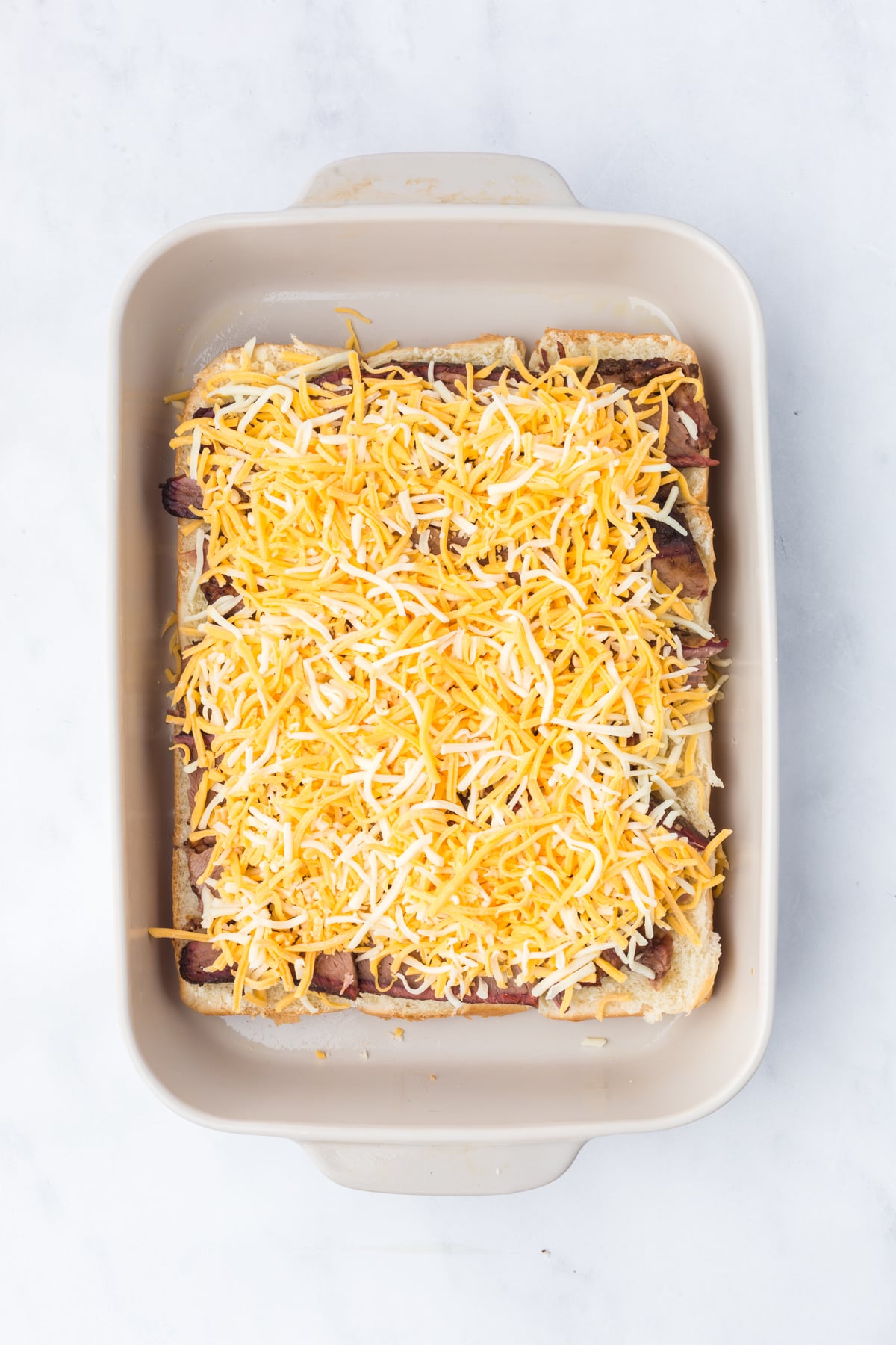 Layers of cheese, brisket, and dill pickles assembled on Hawaiian slider rolls.