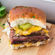 A slider on a cutting board with the rest of the Brisket Sliders in a baking dish in background.