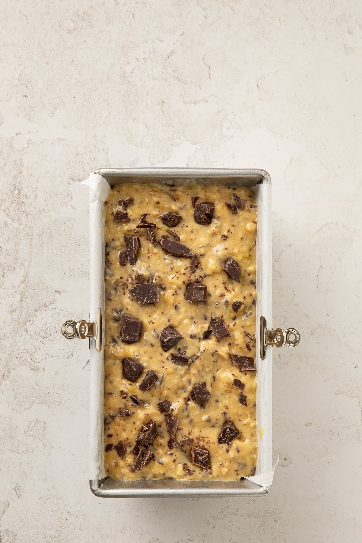 Batter in a parchment-lined loaf pan topped with chocolate chunks.