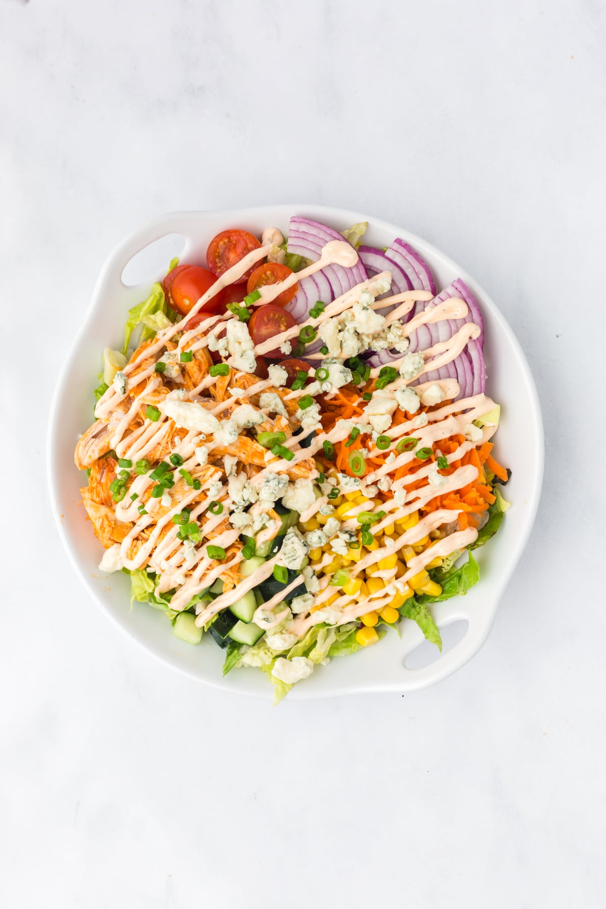 Salad topped with homemade buffalo ranch dressing, blue cheese crumbles, and green onions.