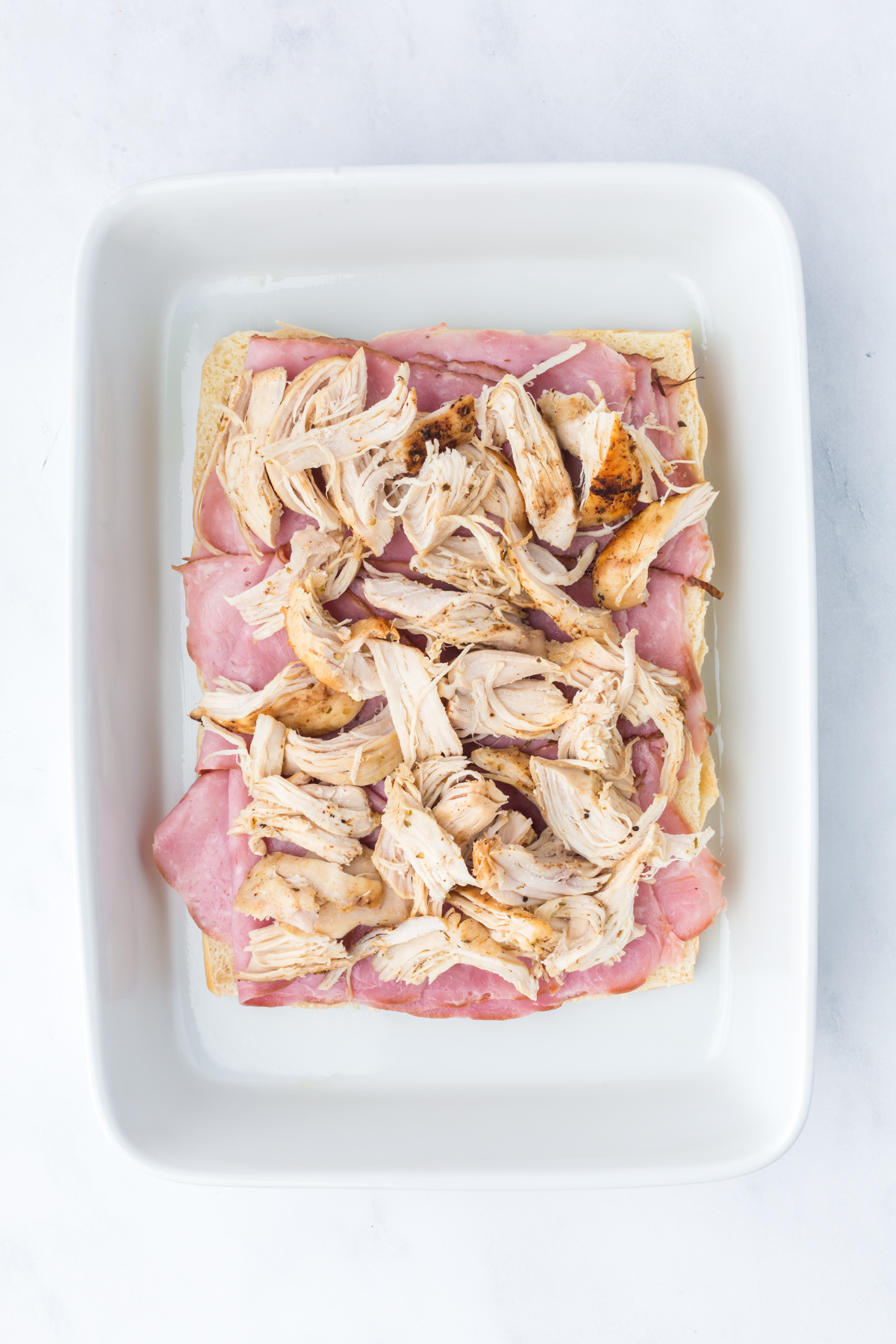 Toasted sliders covered with sliced ham and shredded chicken.