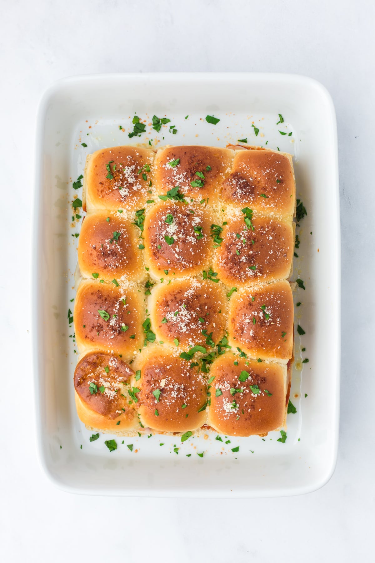 Freshly baked sliders topped with Parmesan cheese and parsley.