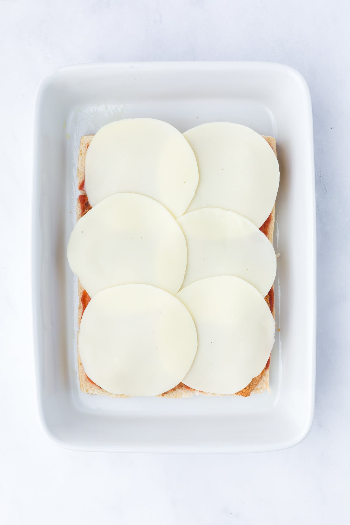 Breaded chicken tenders layered with marinara sauce and provolone cheese for Chicken Parmesan Sliders.