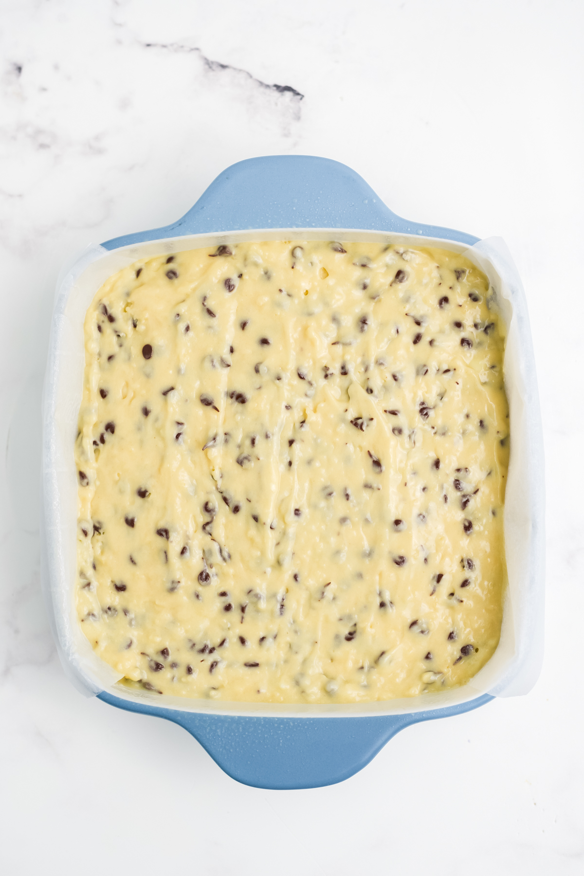 Cake batter spread evenly into a parchment-lined 8x8-inch baking pan before baking.