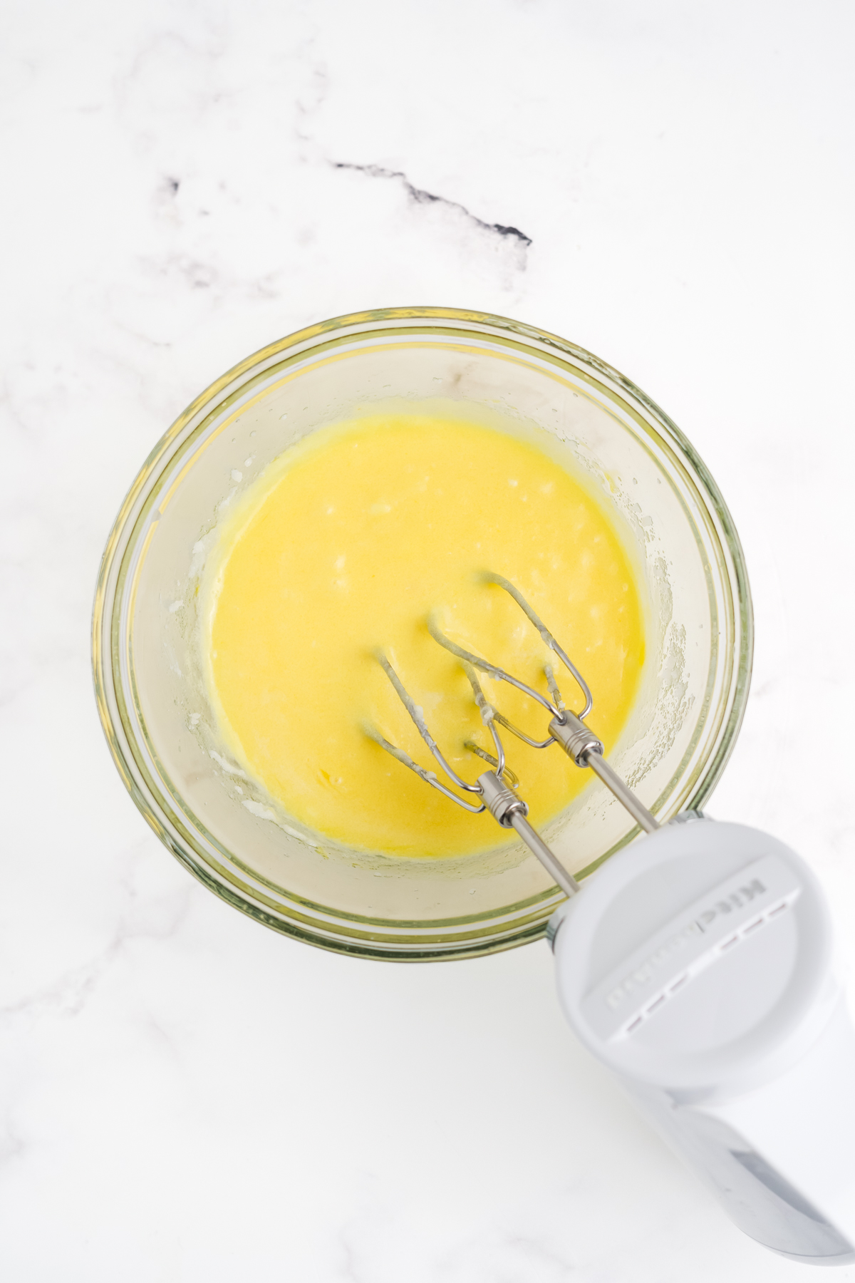 Butter, sugar, eggs, oil, and vanilla in a bowl with a hand blender.