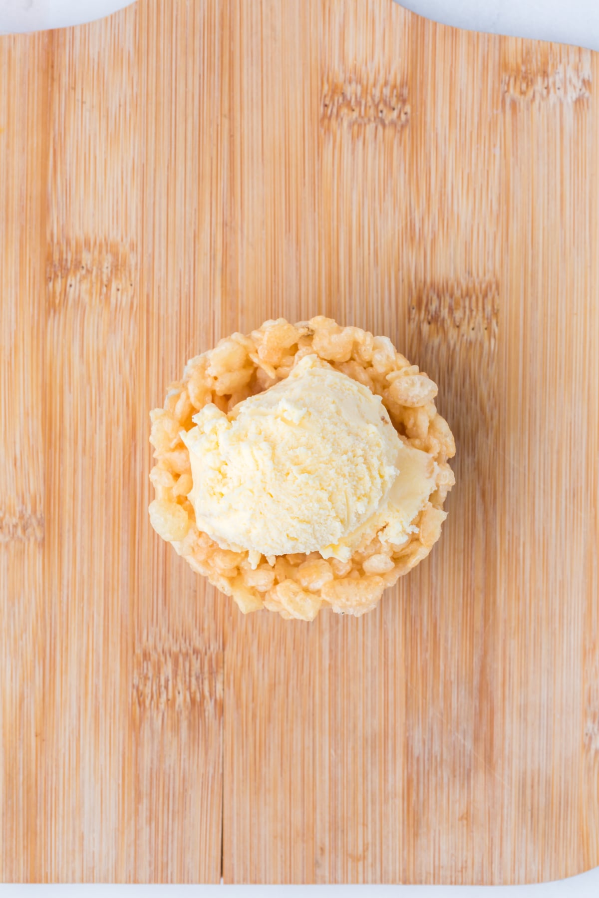 Frozen Rice Krispie bowl on cutting board filled with a scoop of ice cream.