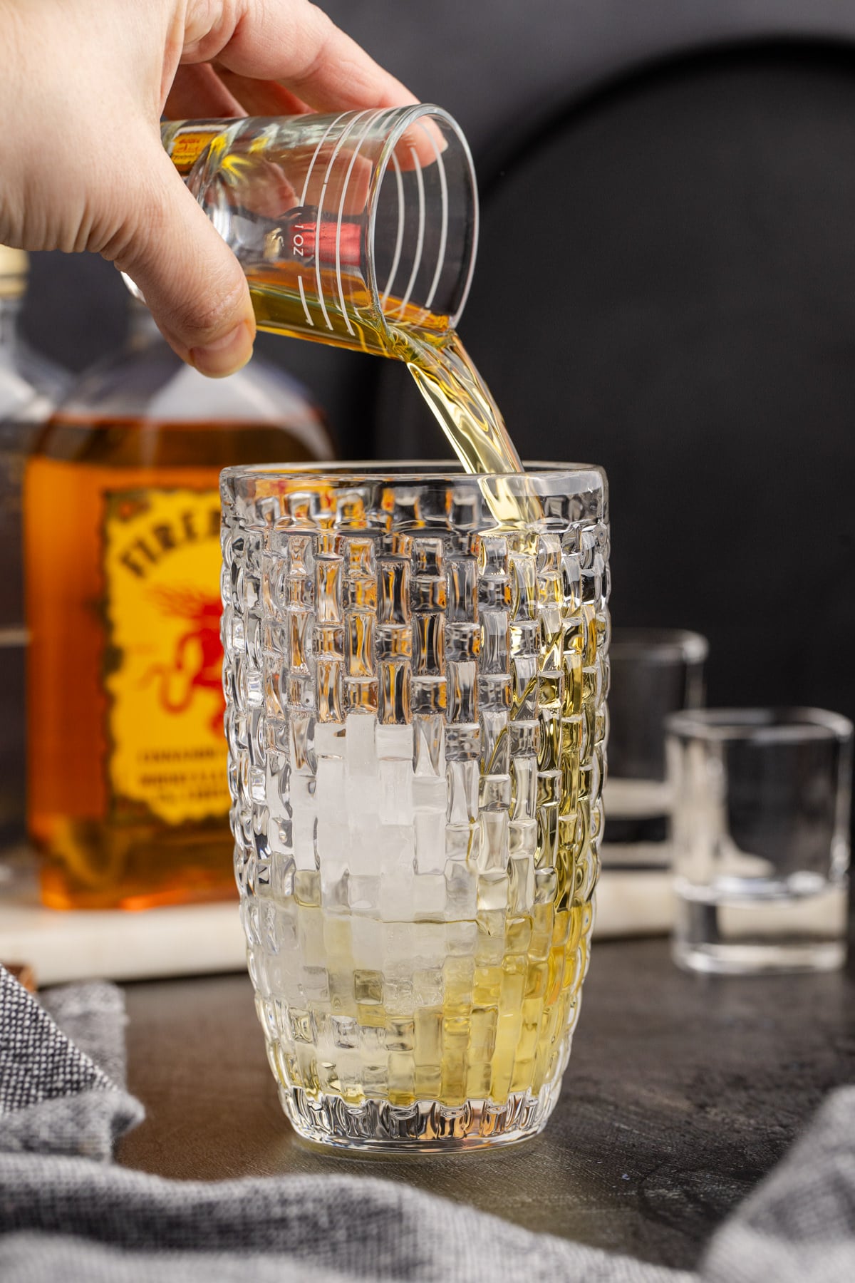 Whiskey being added to cocktail shaker with schnapps and ice.