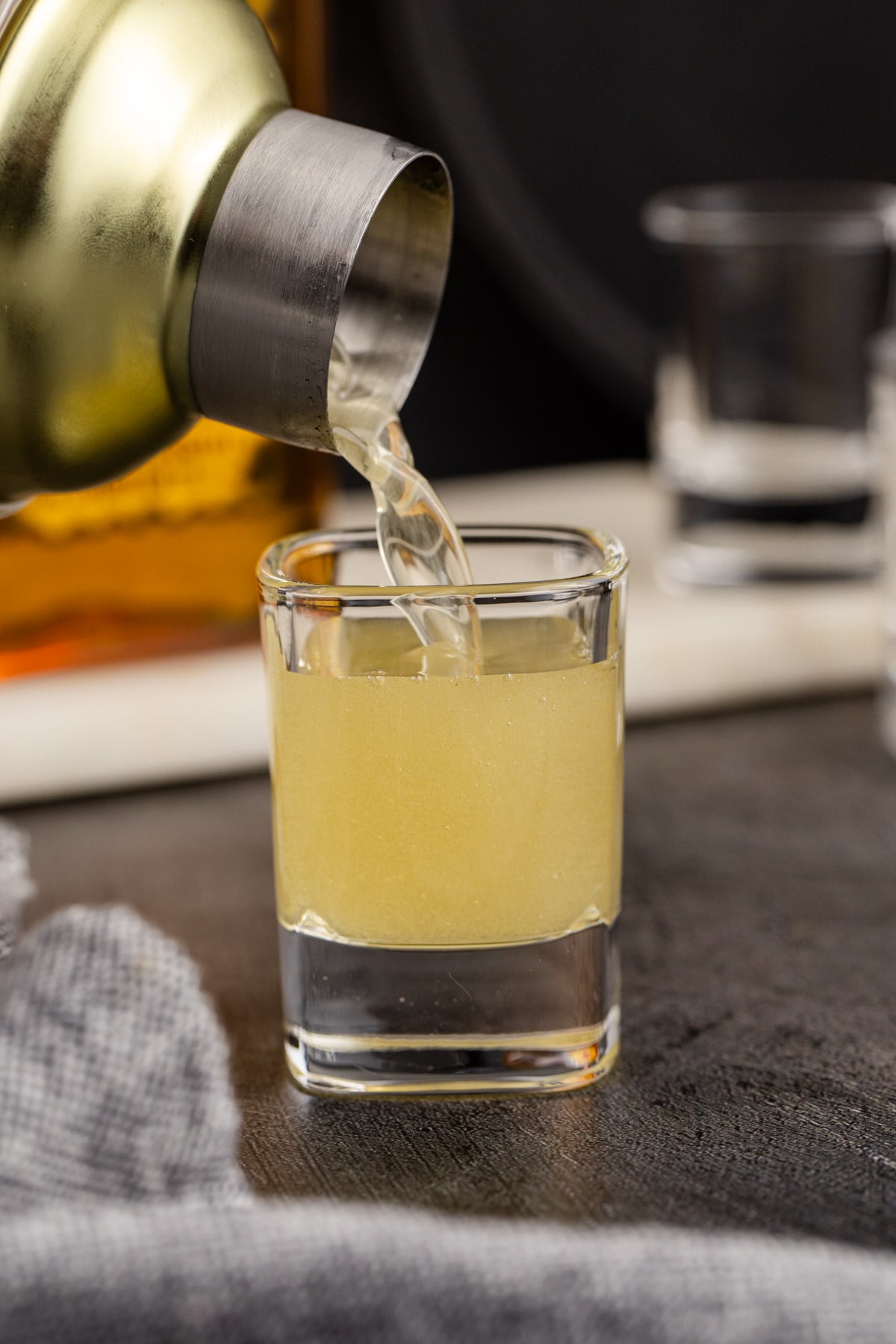 Cocktail shaker pouring chilled drink into shot glass.