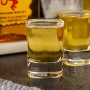A Fire and Ice shot on a table with a bottle of whiskey and another shot in background.