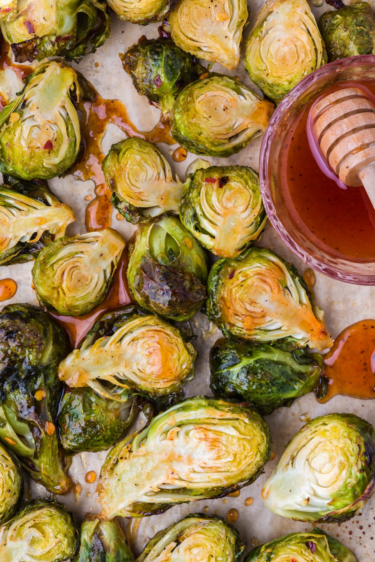 Roasted hot honey glazed Brussels sprouts on a baking sheet with a bowl of hot honey that was freshly drizzled.