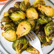 A pile of roasted hot honey Brussels Sprouts in a serving bowl with a fork lifting one out.