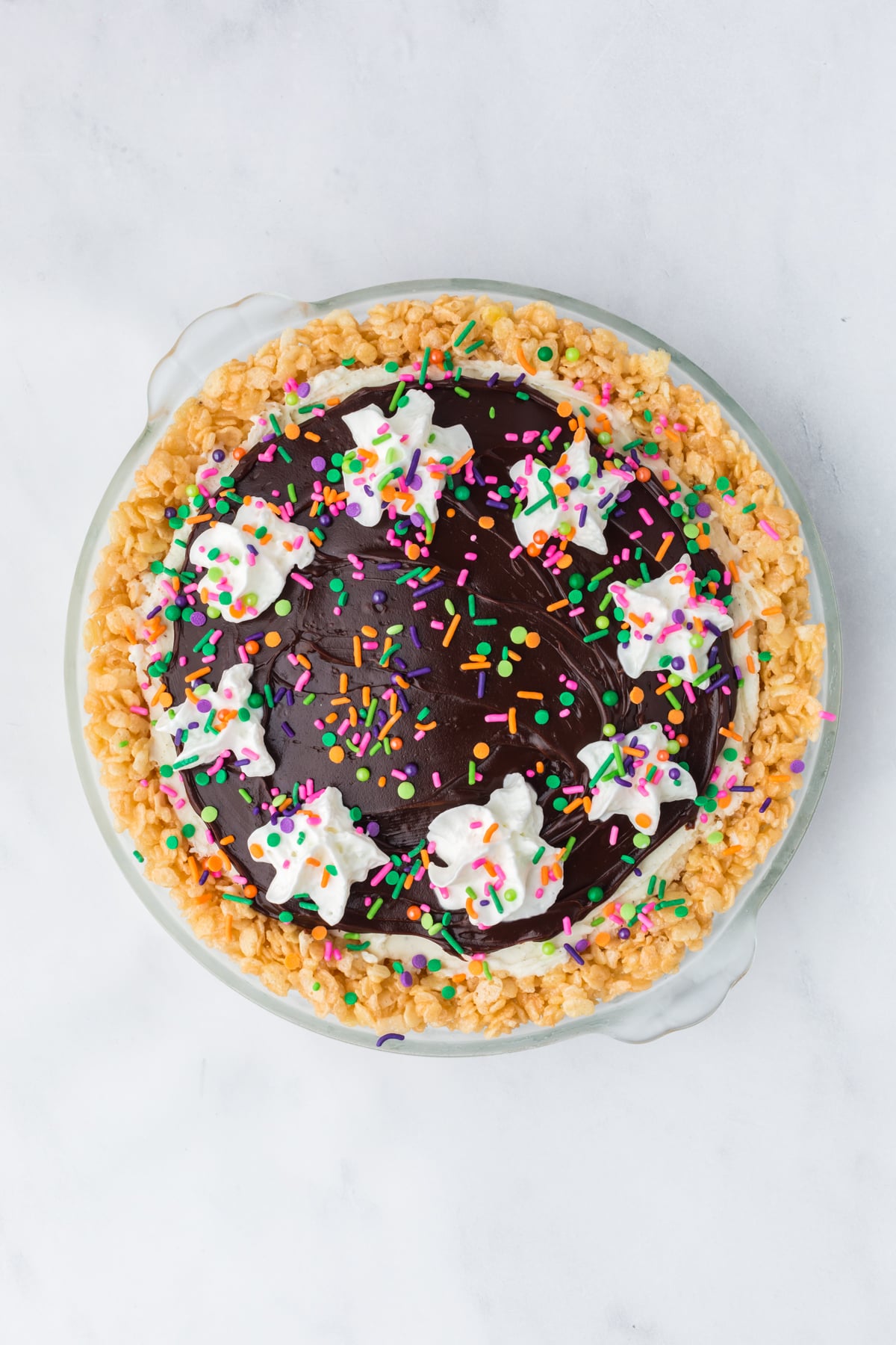 Hot fudge topping added to pie with whipped cream dollops and sprinkles.