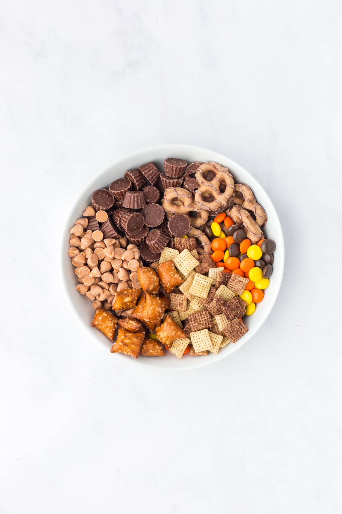 Chocolate Chex cereal, Reese's Minis, Reese's Dipped Pretzels, Reese's Pieces, Reese's Peanut Butter Chips, and pretzel bites in a large mixing bowl.