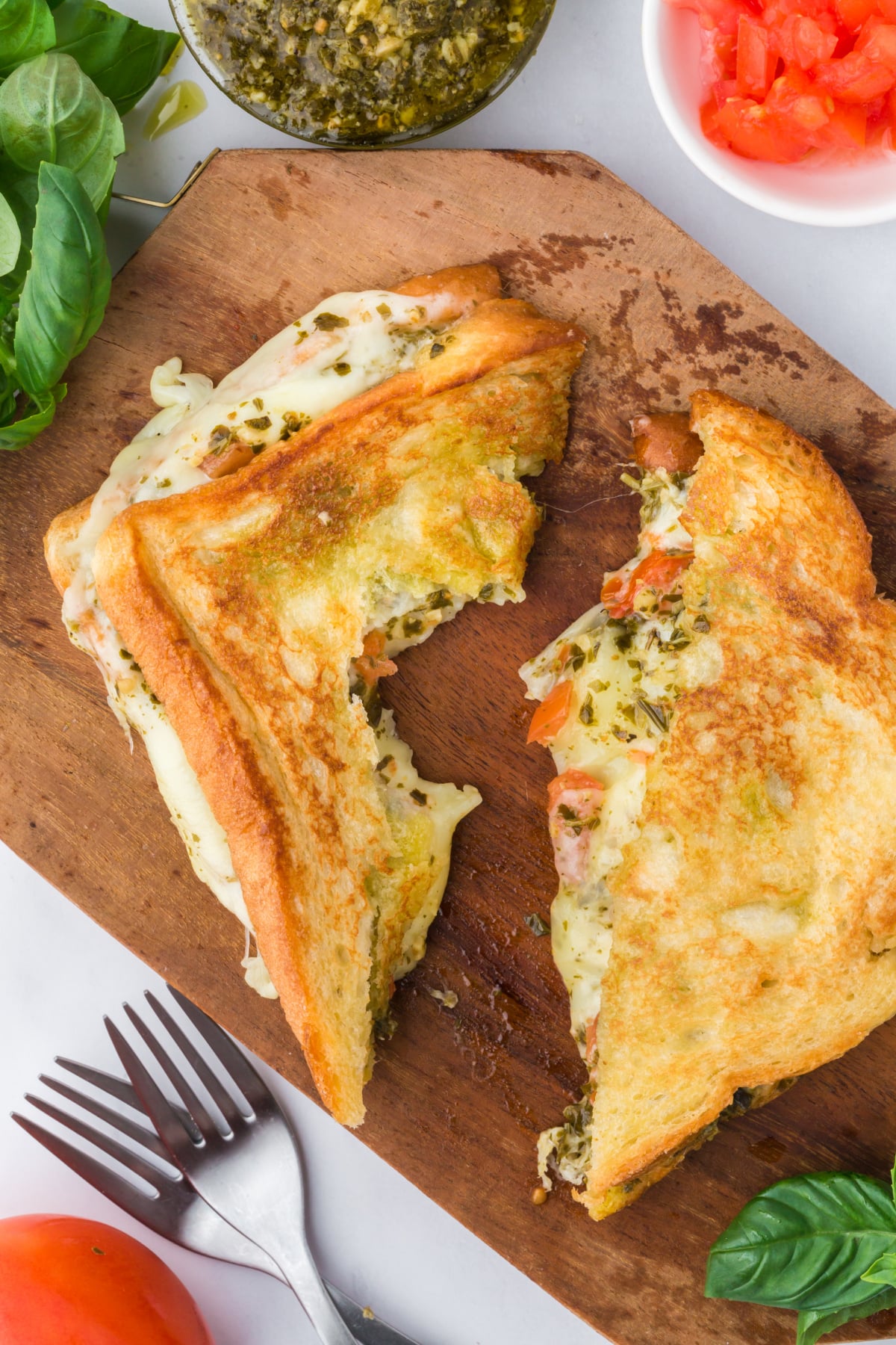 A grilled cheese cut in half on a cutting board with one half missing a bite.