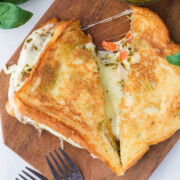 A freshly made pesto grilled cheese on a cutting board cut in half with one half missing a bite.
