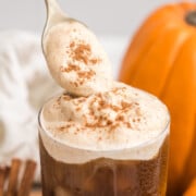 A Pumpkin Cream Cold Brew with a spoon lowering more pumpkin cold foam sprinkled with pumpkin pie spice on top.