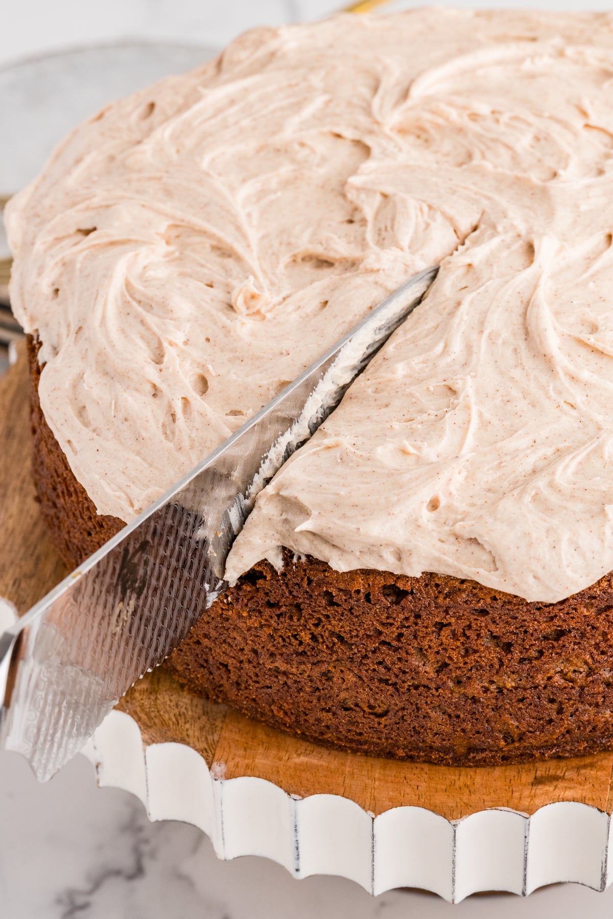 Frosted cake on serving plate with a knife starting to slice it.