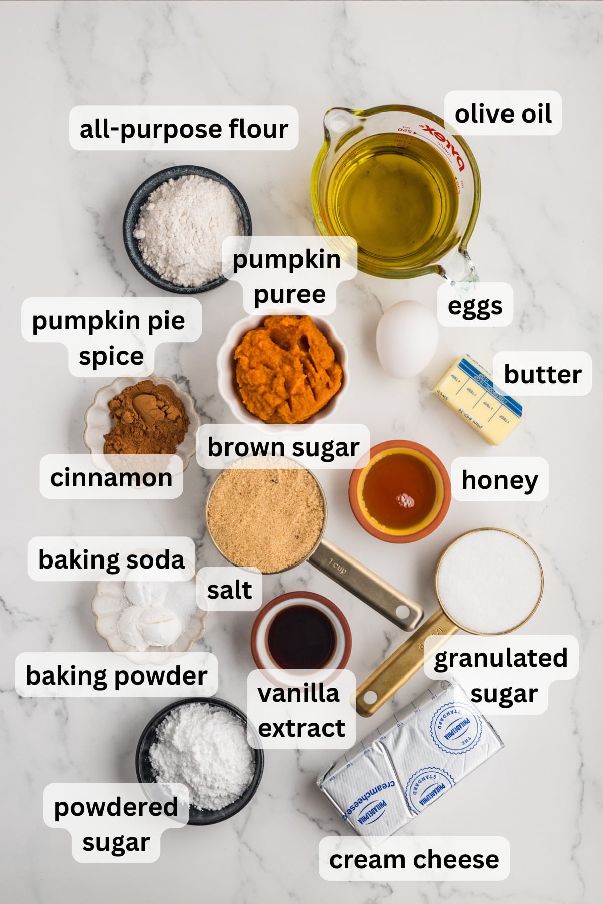 All of the ingredients needed to make pumpkin olive oil cake and cinnamon cream cheese frosting in bowls on a table.