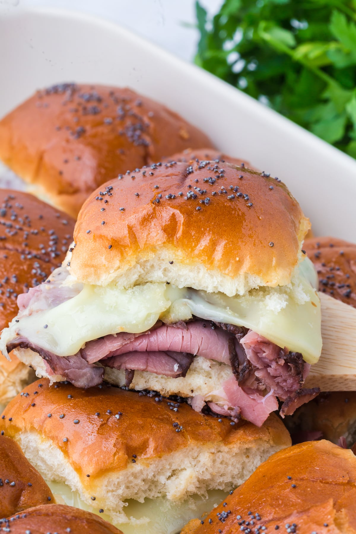 Freshly baked sliders in a casserole dish with one on top.