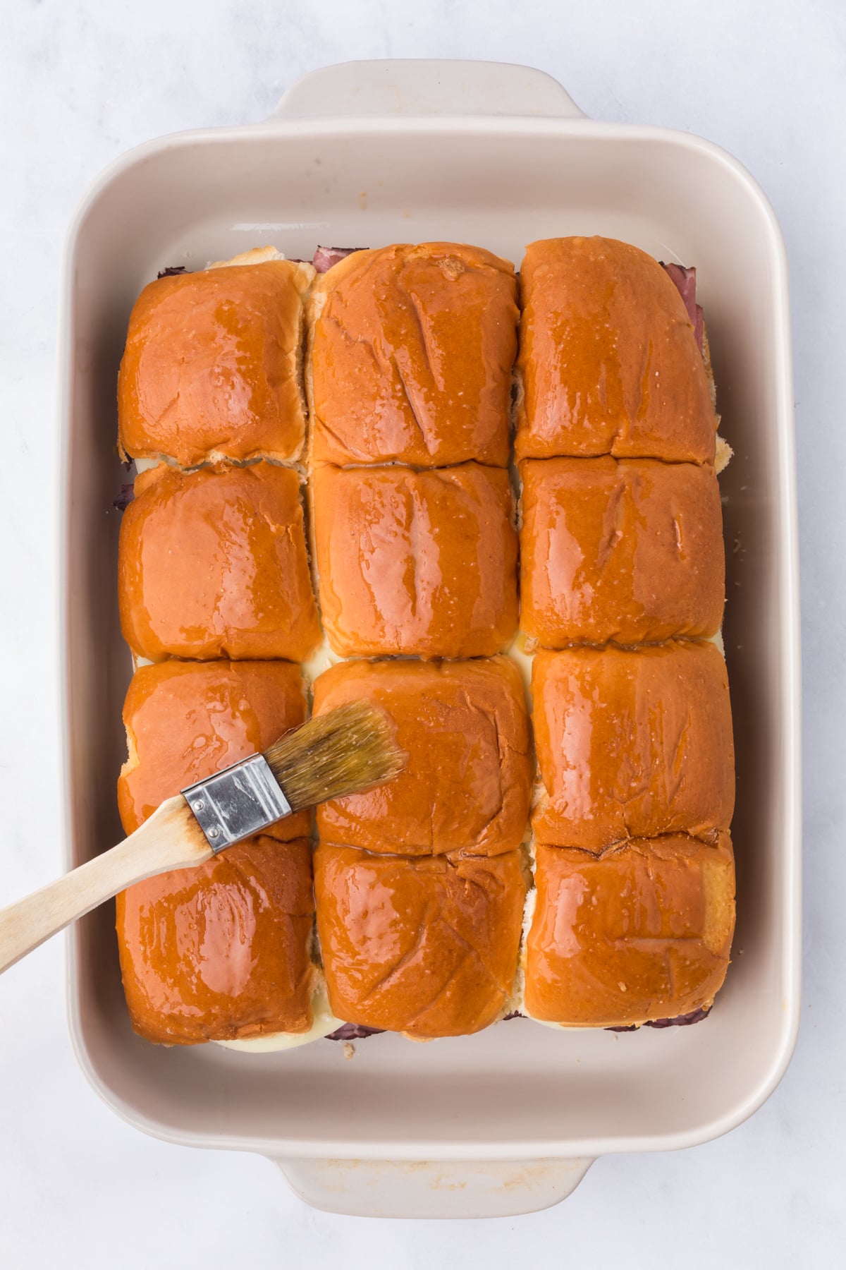 Butter mixture being brushed on top of sliders.