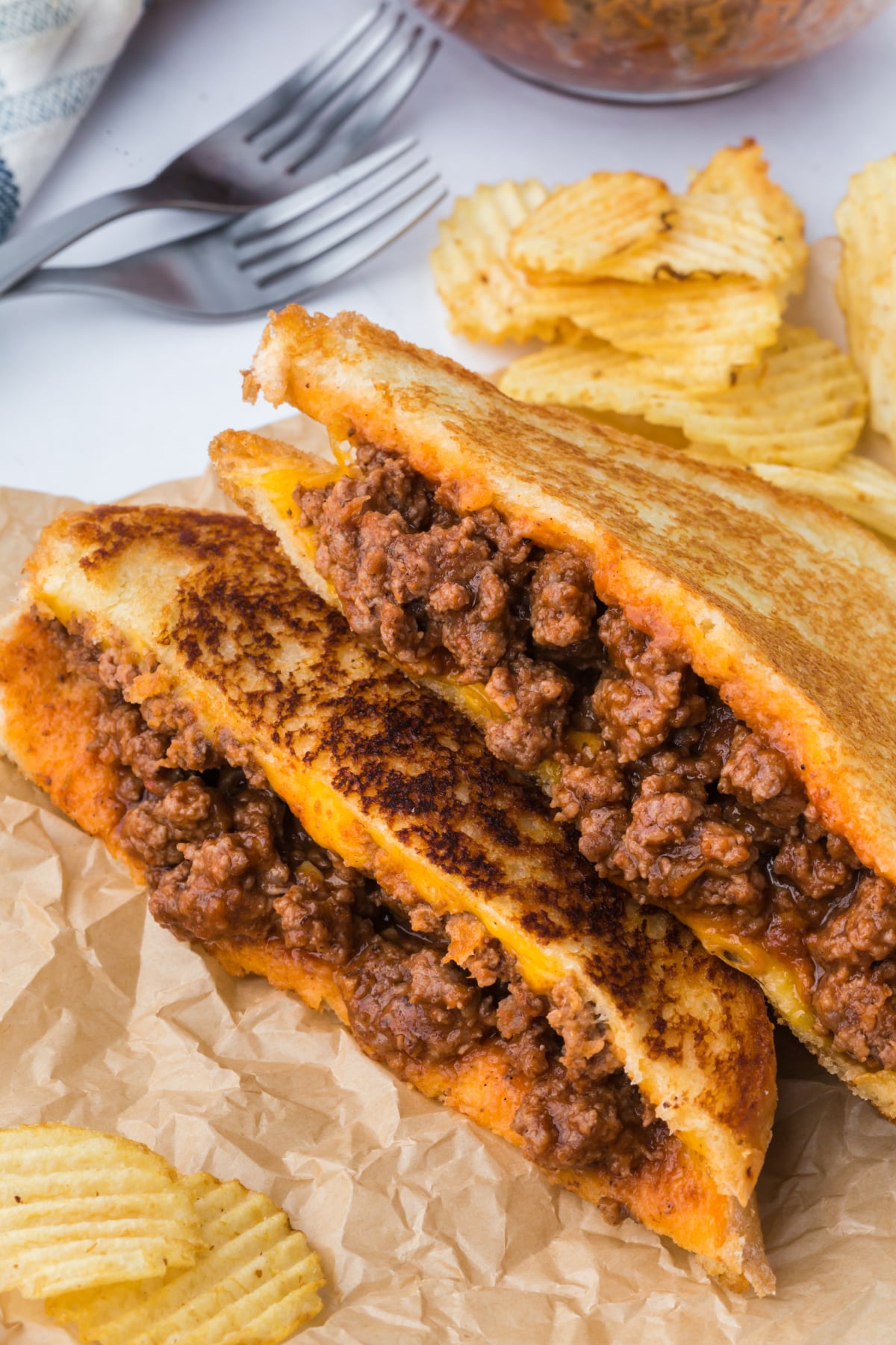 Two grilled cheese halves on top of each other on parchment with chips.