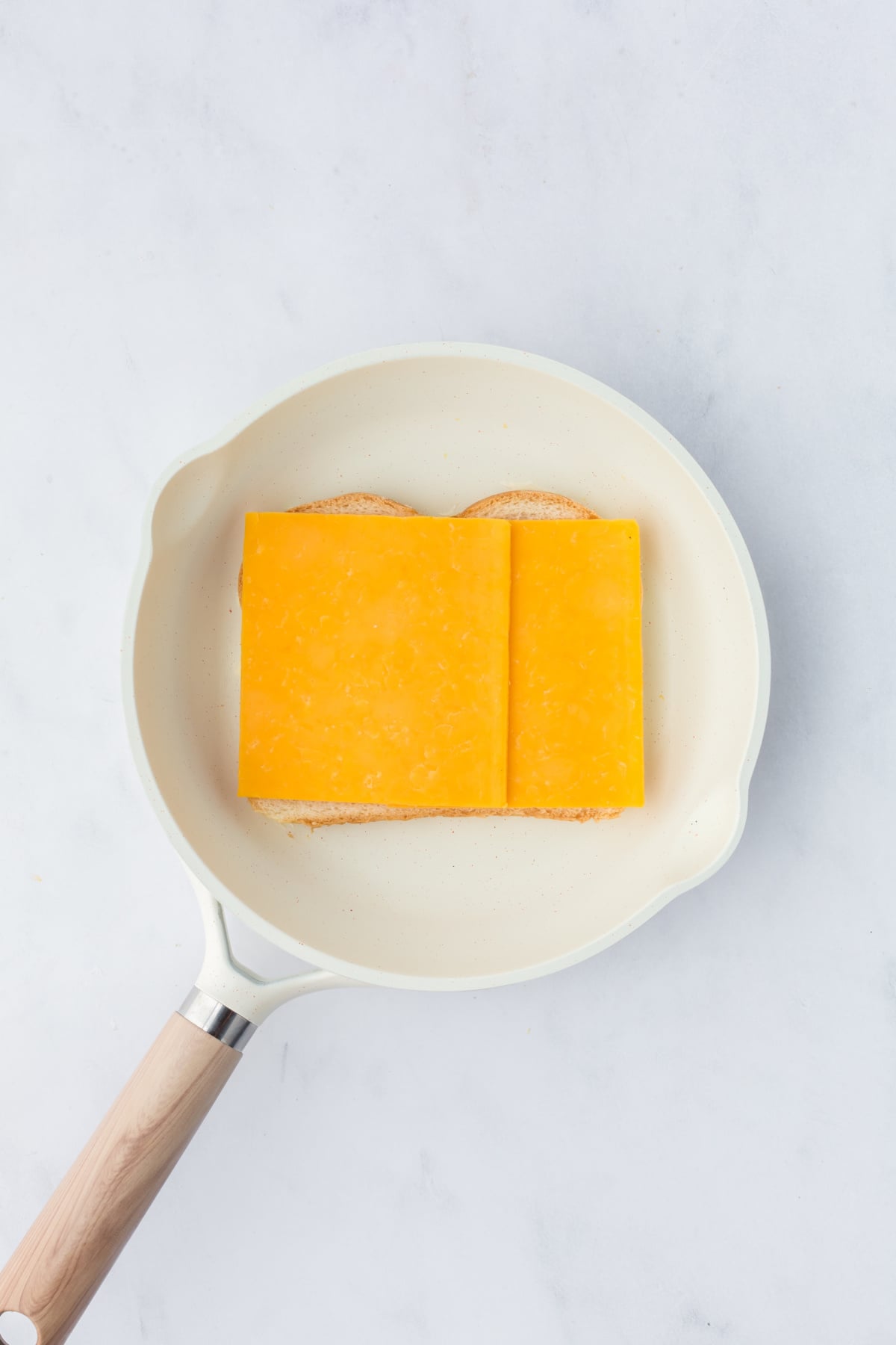 Cheddar cheese on buttered bread in skillet.