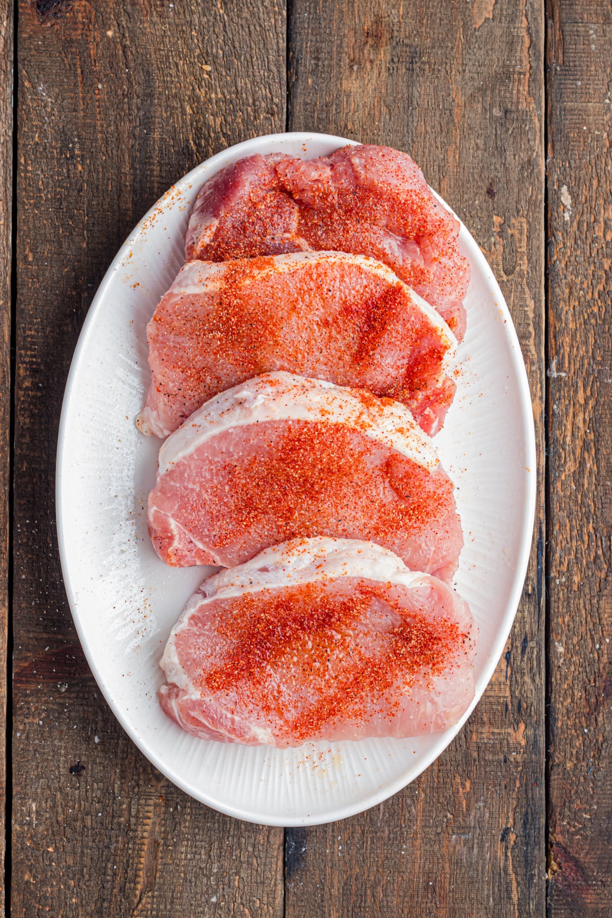 Seasoning added on to pork chops on a plate.