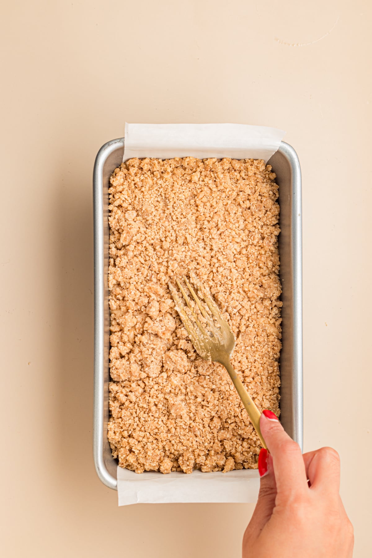 Streusel added on top of banana bread batter in parchment covered pan on table.