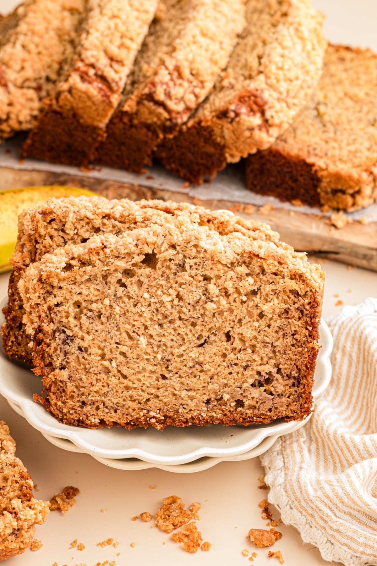 Slice of banana bread with streusel topping on its edge leaning on two others on a plate.