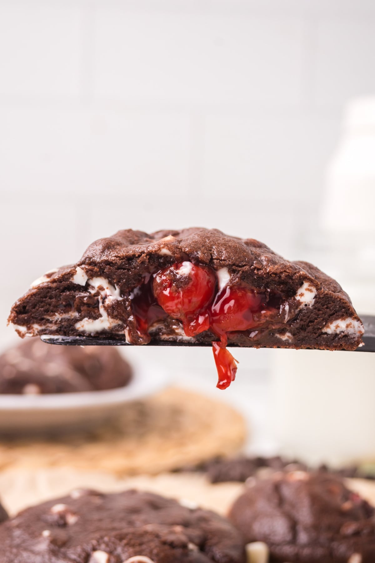 A half of a cherry stuffed chocolate cookie showing the inside being held up in the air.