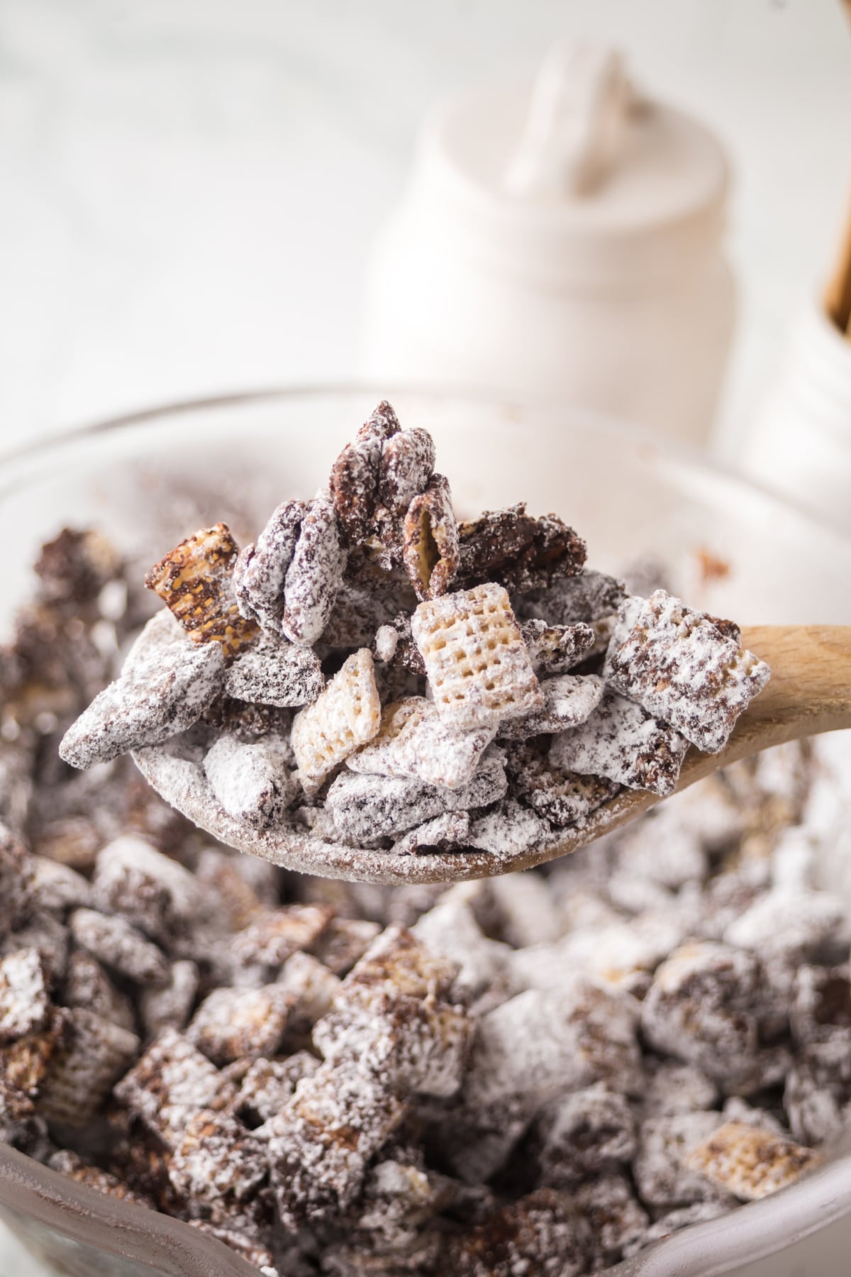 A wooden spoonful of Chex cereal held above a bowlful.