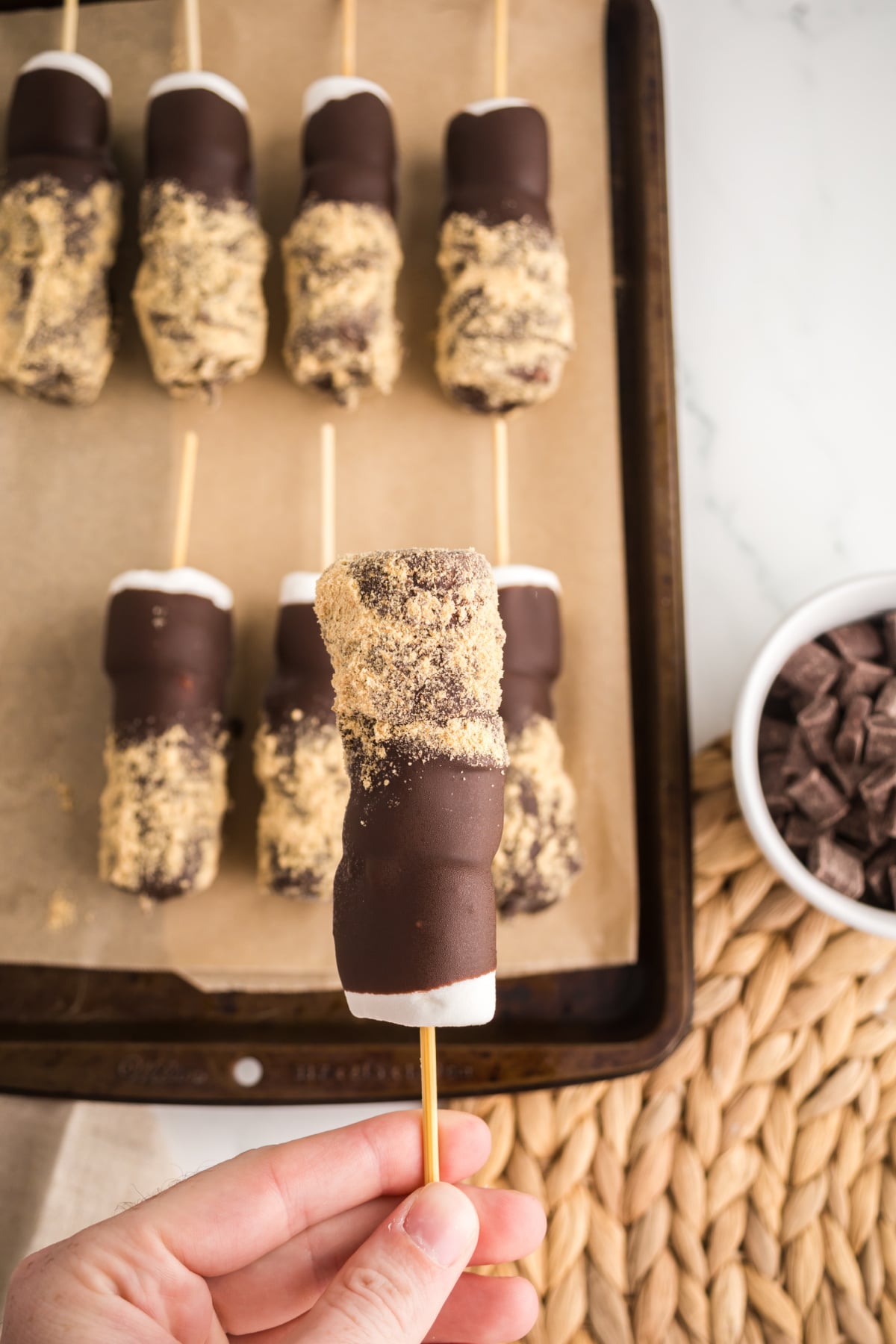 A skewer held above a baking sheet full of chilled skewers.