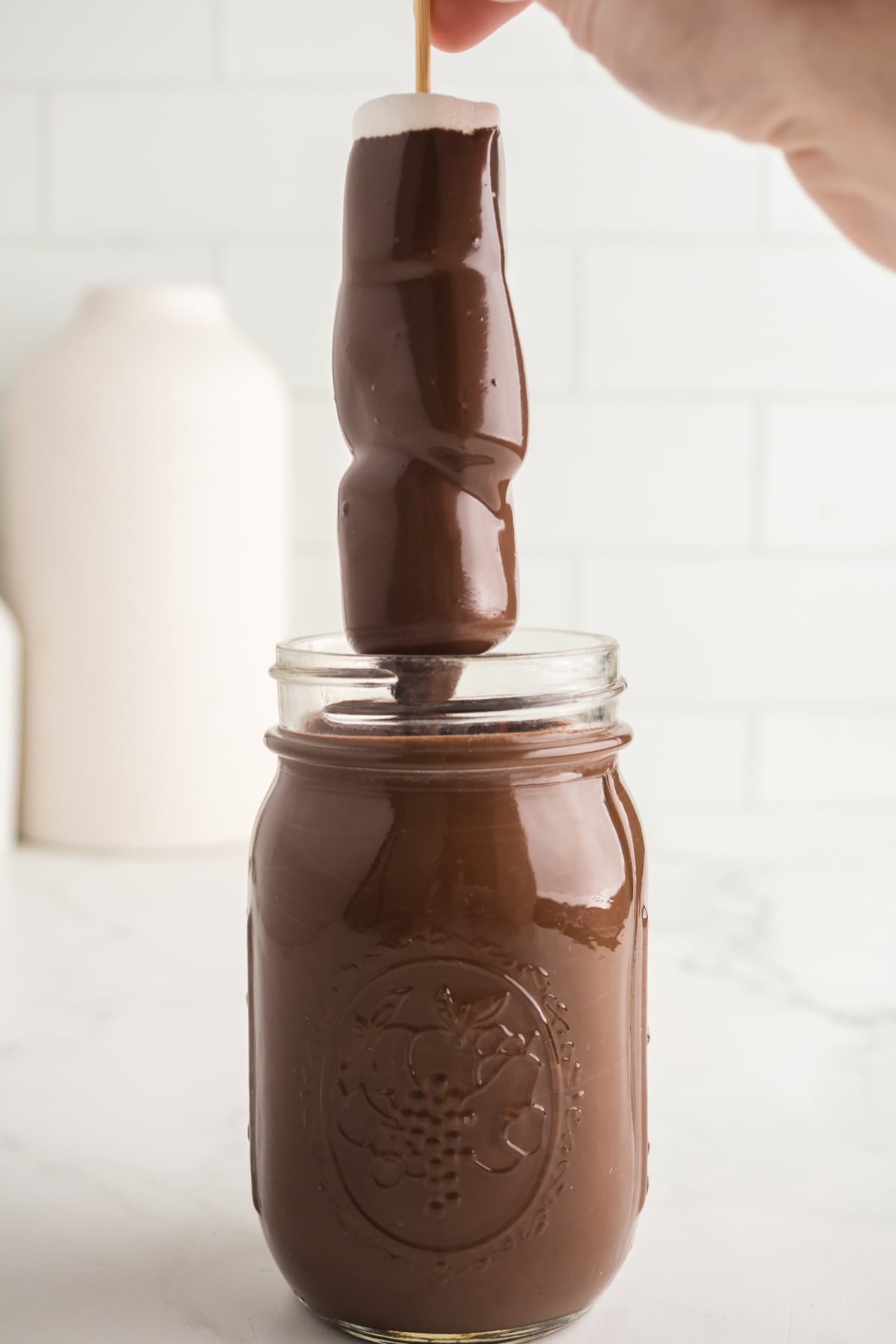 A skewer with 3 marshmallows dipped in melted chocolate.
