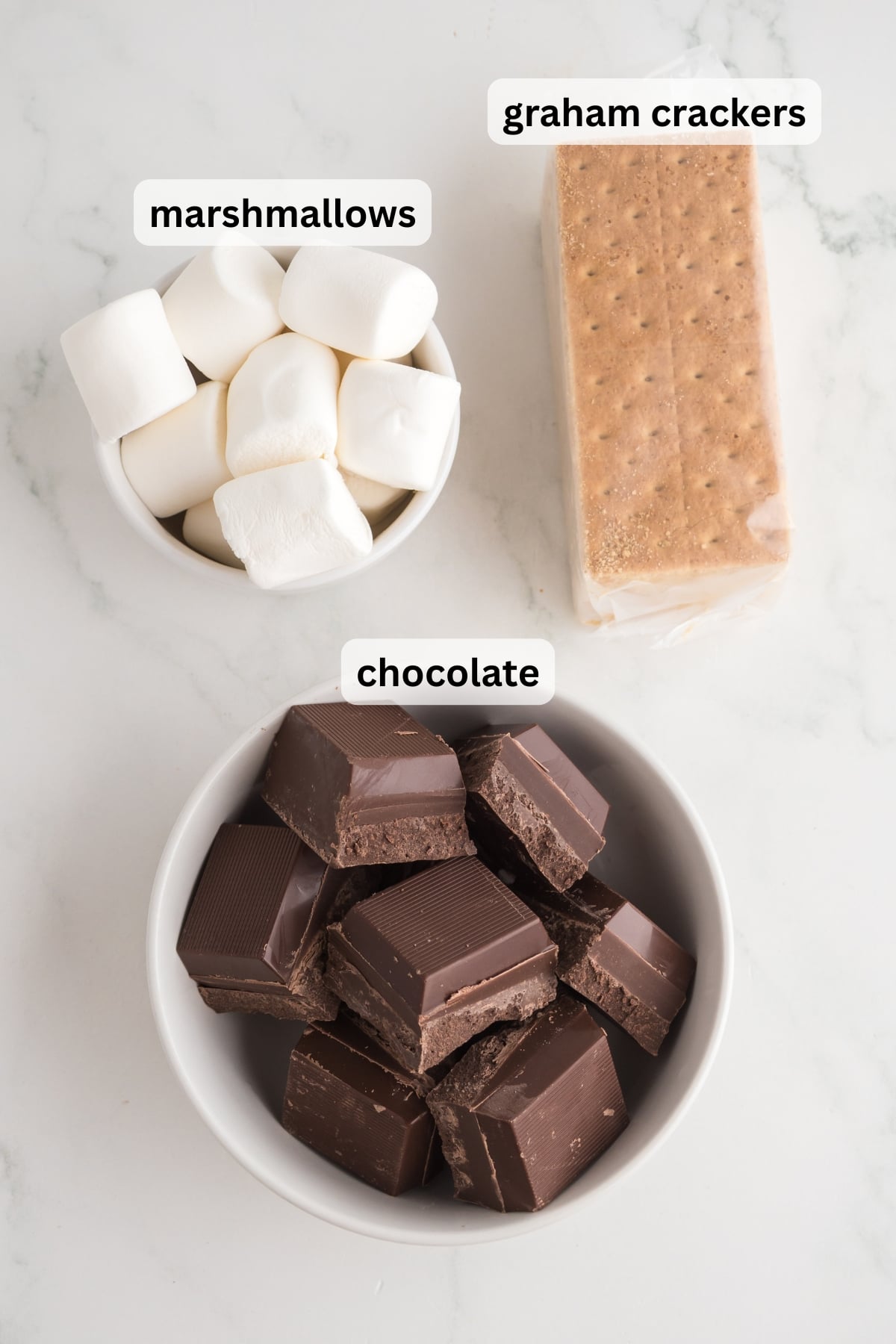 All of the ingredients needed to make s'mores skewers in bowls on a table.