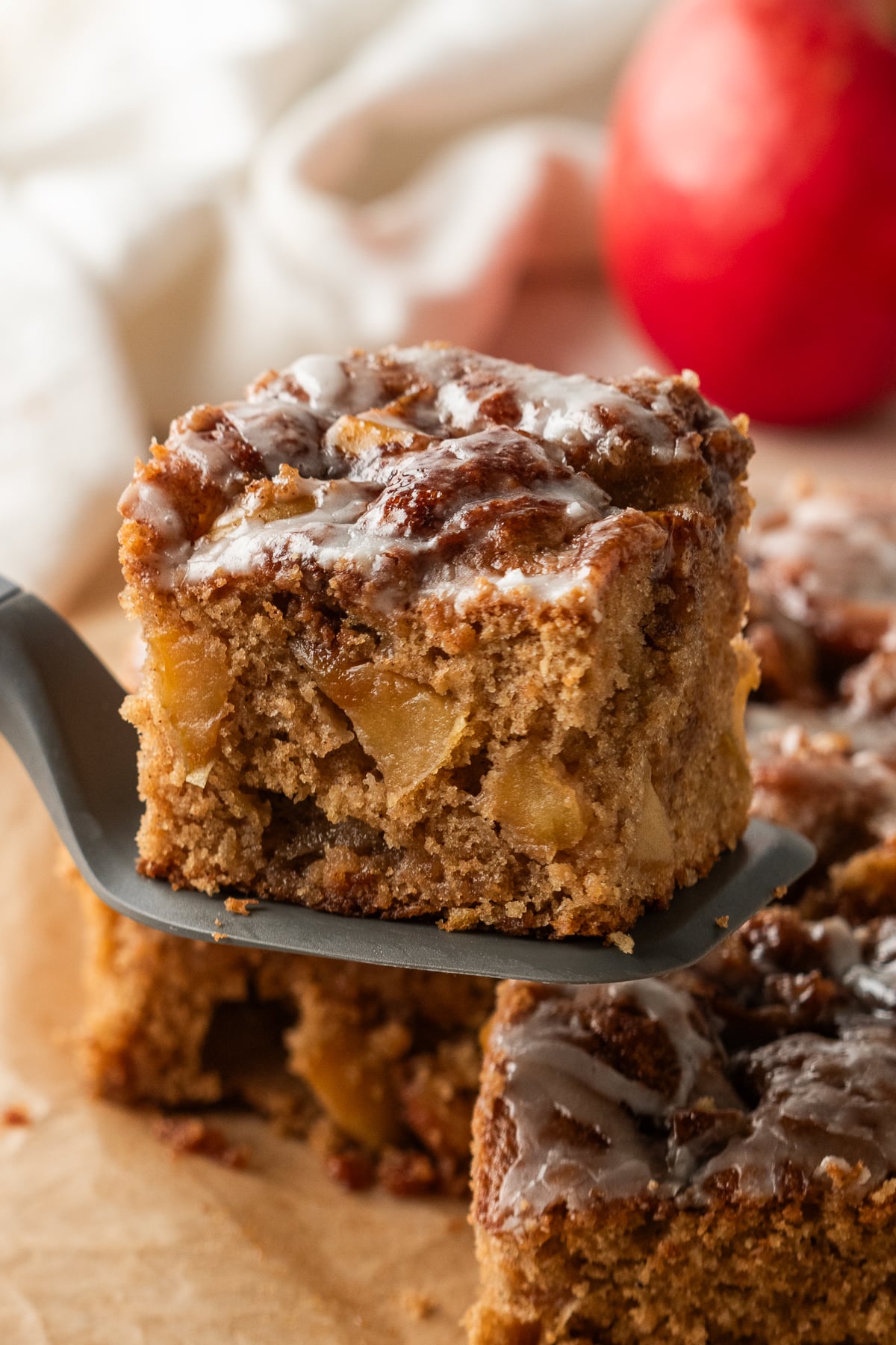 A slice of cake on a spatula in the air showing tender cinnamon apples throughout the crumb.