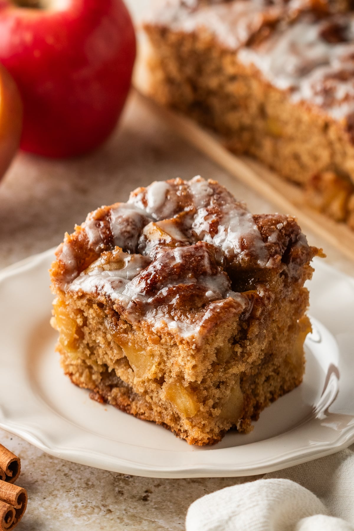 A slice of cake topped with cinnamon apples and vanilla glaze on a plate.