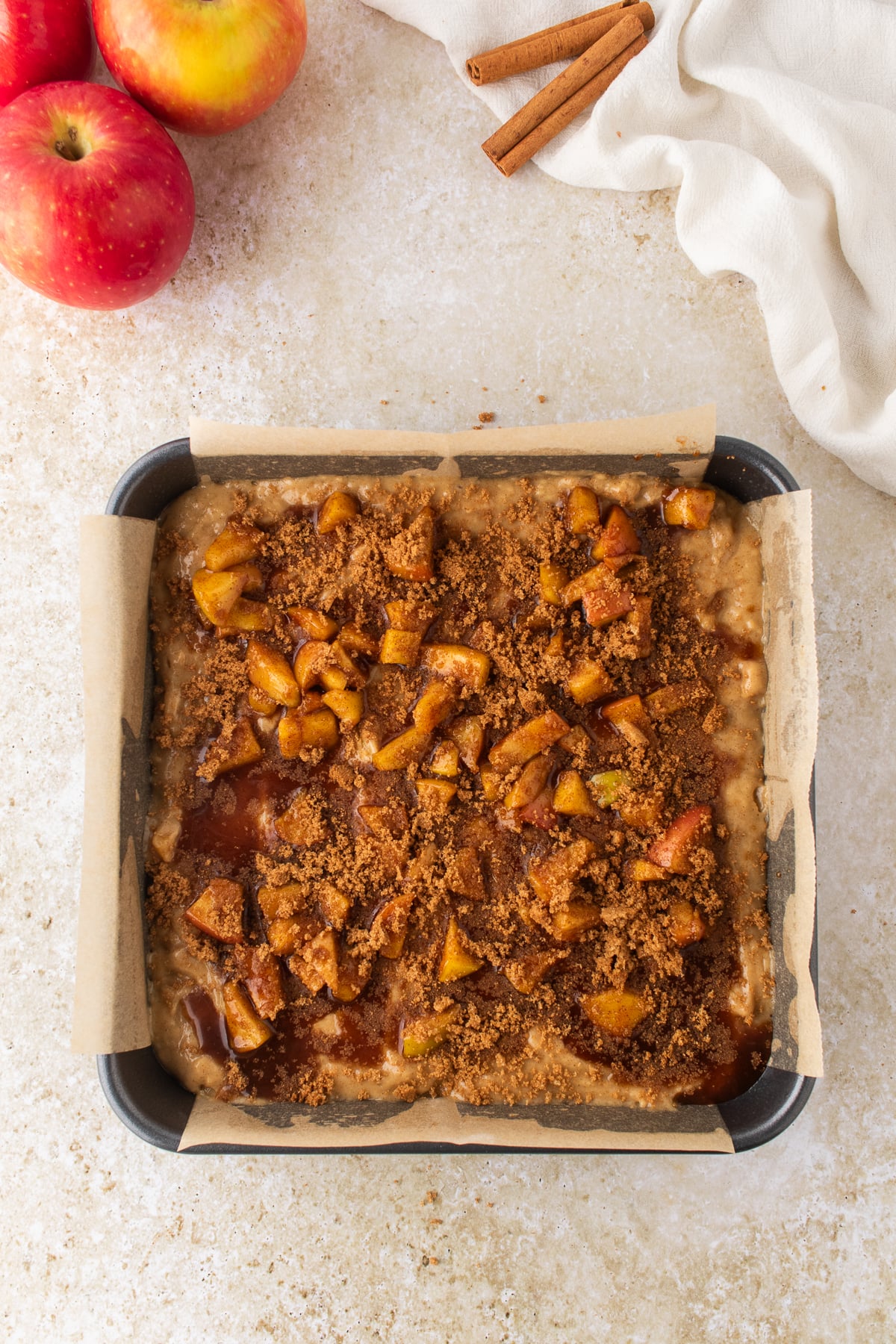Cake batter topped with cinnamon apples and brown sugar in a square baking pan.