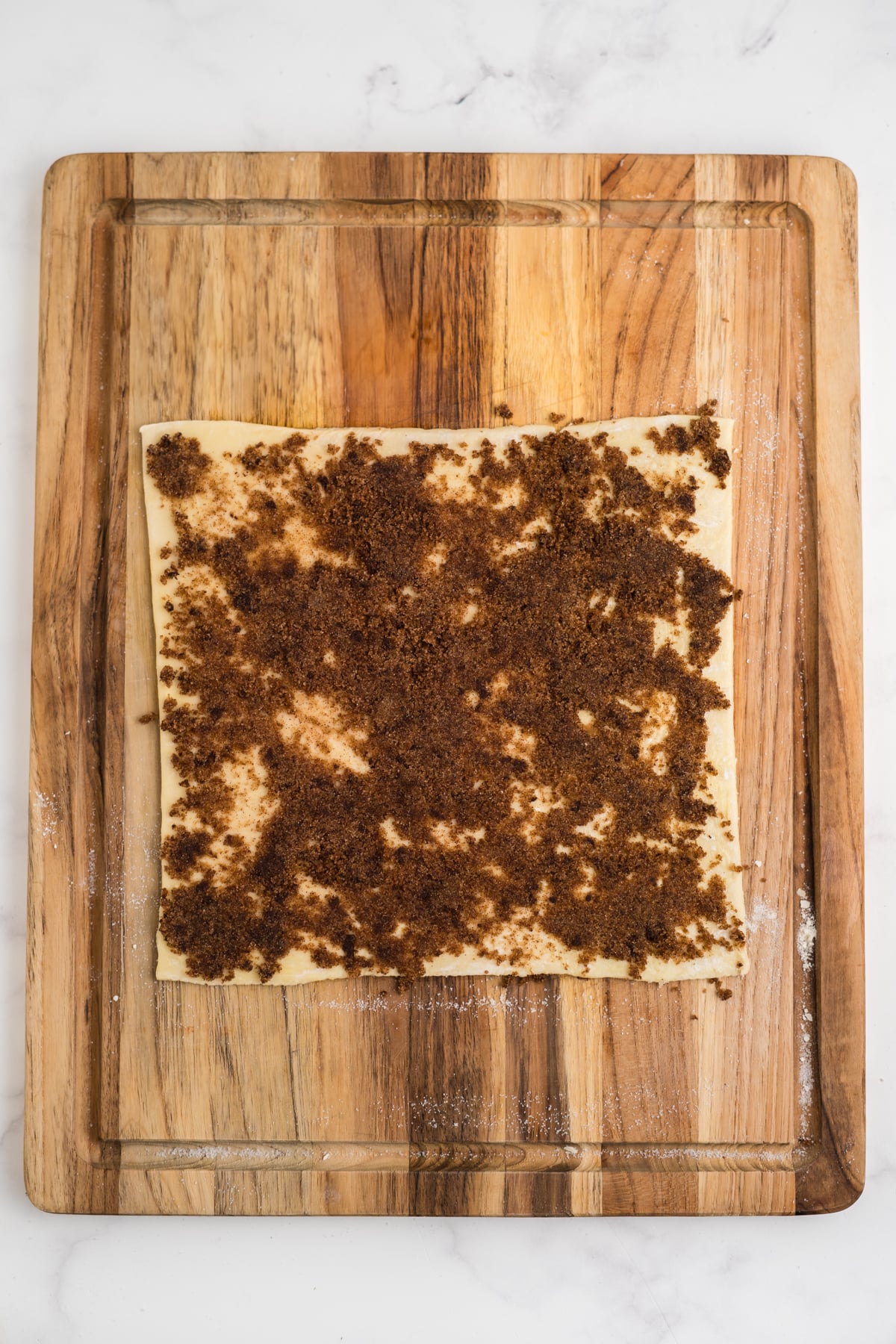 Puff pastry on cutting board topped with buttery cinnamon sugar filling almost to the edge.