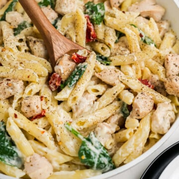 A wooden spoon lifting a spoonful of Creamy Garlic Chicken Pasta up to edge of the serving bowl.