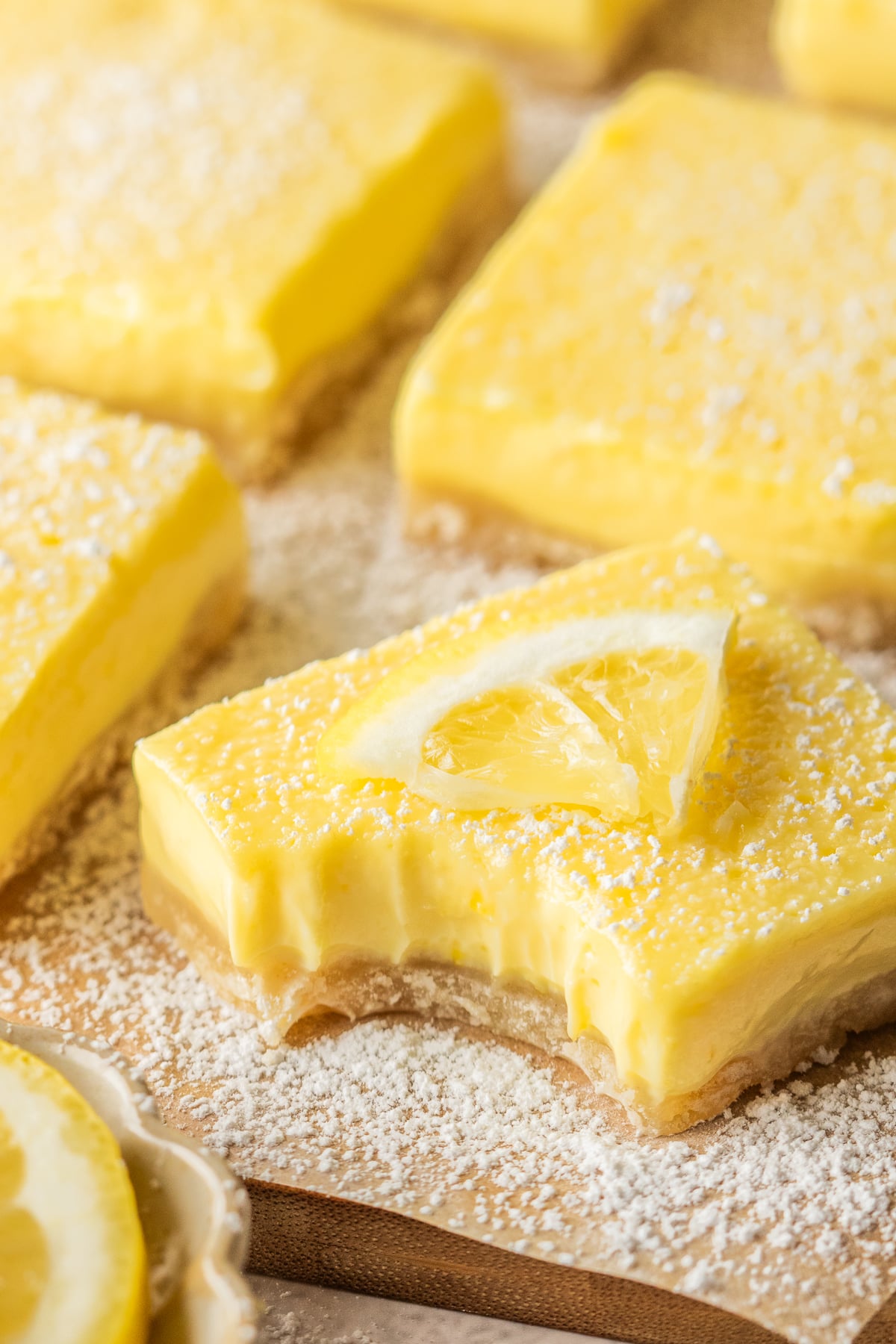 Garnished lemon bars on parchment with one missing a bite.