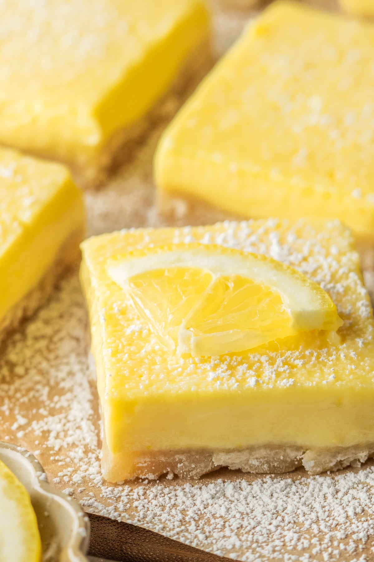Lemon Bars on a cutting board dusted with powdered sugar and garnished with lemon slices.